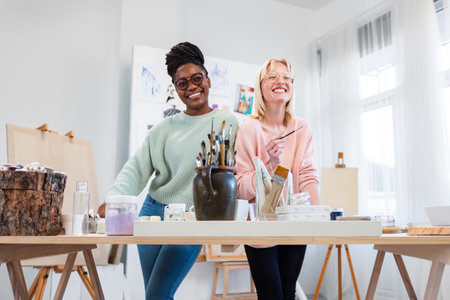 Portrait of smiling female artist with colleague standing at table in studioの写真素材