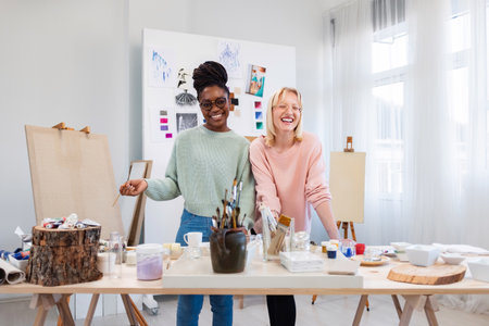 Portrait of happy female artist and her colleague standing at table in studioの写真素材
