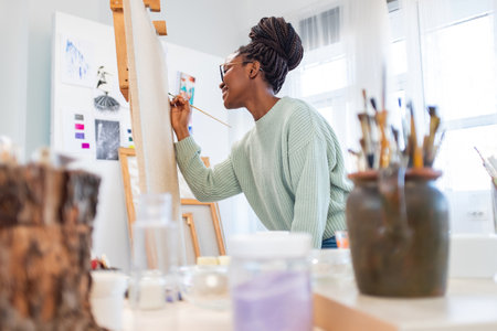 Young african-american woman painting on canvas in art studioの写真素材