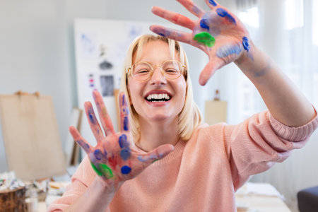 Smiling female artist showing her hands painted in bright colors at studioの写真素材