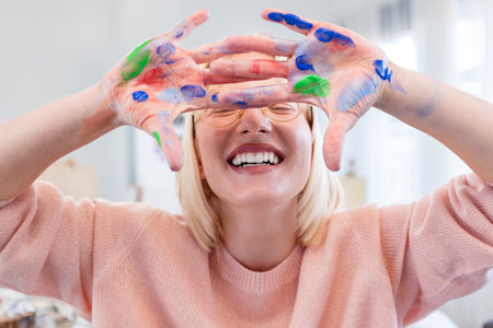 Happy woman with hands painted in colorful paints smiling at camera at homeの写真素材