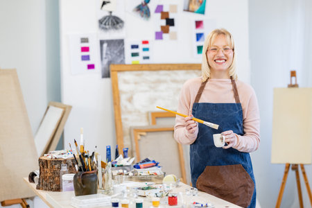 Portrait of smiling female artist standing in her studio and holding paintbrushの写真素材