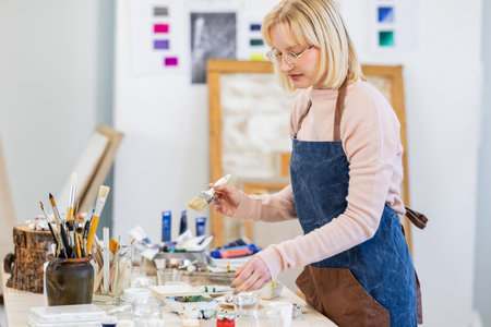 Senior female artist painting on canvas in her studio. She is wearing apron and apron.の写真素材