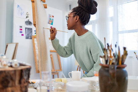 african american woman painting picture on easel at art studioの写真素材