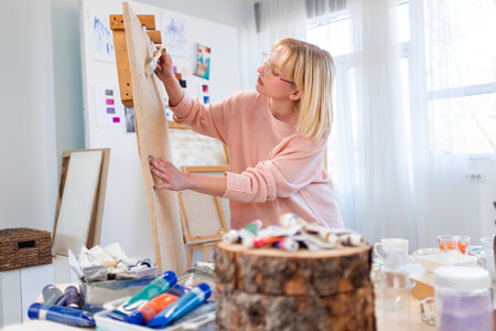 Woman painting a picture in her art studio. She is wearing a pink sweater.の写真素材