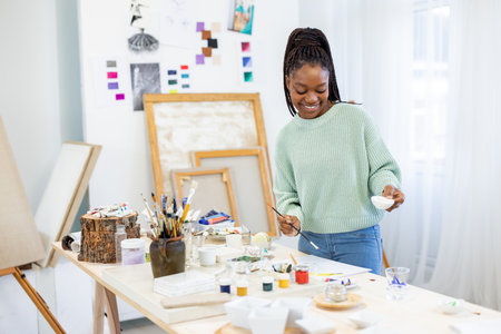 happy african american woman painting picture in art studio at homeの写真素材