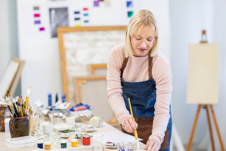 Portrait of a mature female artist painting on canvas in her studioの写真素材