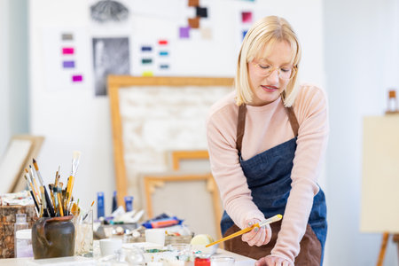 Portrait of mature female artist painting on canvas in art studio.の写真素材