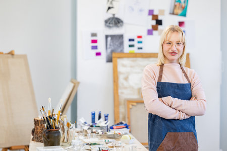Portrait of mature female artist standing with arms crossed in art studioの写真素材