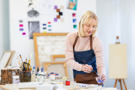 portrait of smiling female artist painting picture on canvas in art studioの写真素材