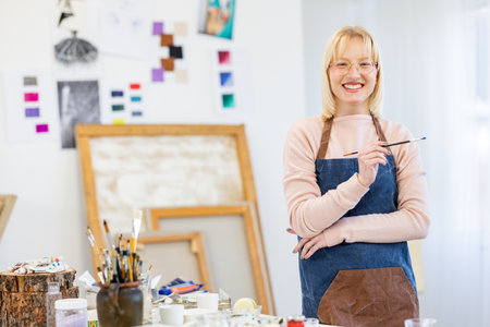 Portrait of smiling female artist standing with paintbrush in art studioの写真素材