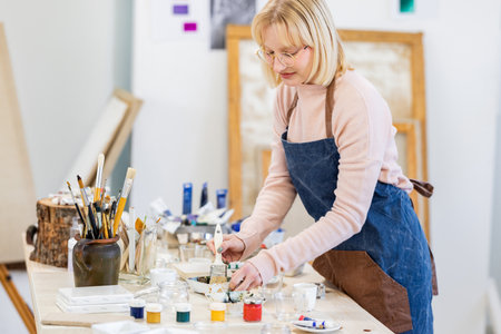 Senior woman painting on canvas in art studio. She is wearing apron and apron.の写真素材