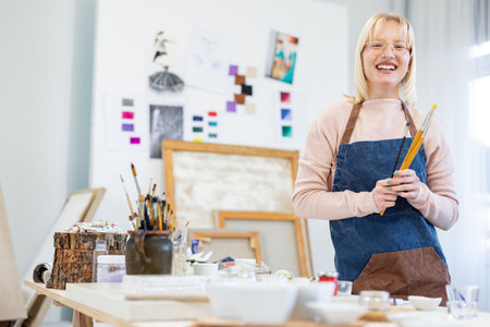 Portrait of smiling mature female artist holding paintbrush in her workshopの写真素材