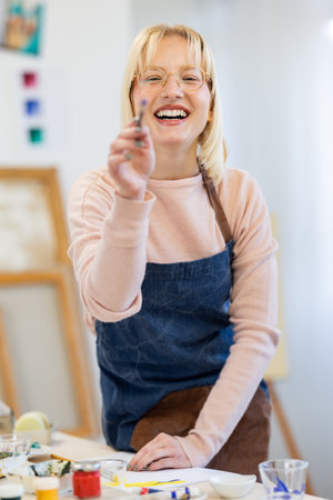 Portrait of smiling female artist with paintbrush and palette in workshopの写真素材