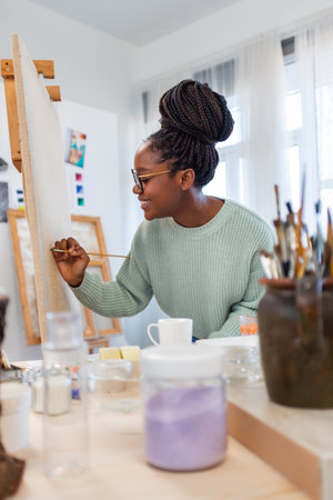 african american woman in eyeglasses painting picture in art studioの写真素材