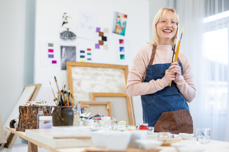 Portrait of smiling female artist holding paintbrush while standing in workshopの写真素材