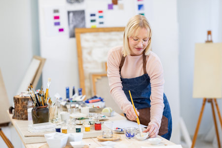 Portrait of mature female artist painting picture on canvas in her studioの写真素材