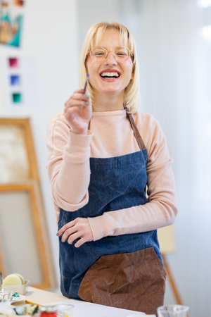 Portrait of smiling female artist standing in workshop and holding paintbrushの写真素材