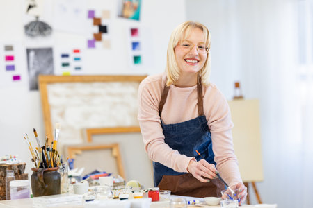 Portrait of smiling female artist in apron working with paints in studioの写真素材