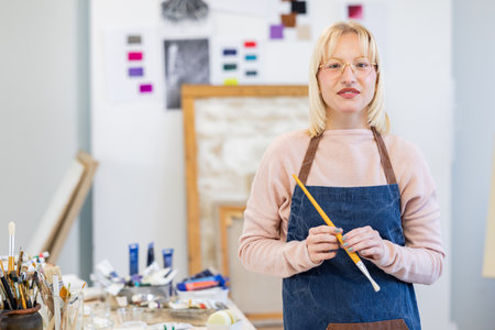 Portrait of mature female artist standing with paintbrush in her workshopの写真素材