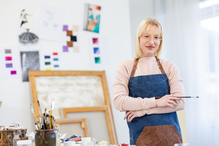 Portrait of mature female artist in apron standing in art studioの写真素材