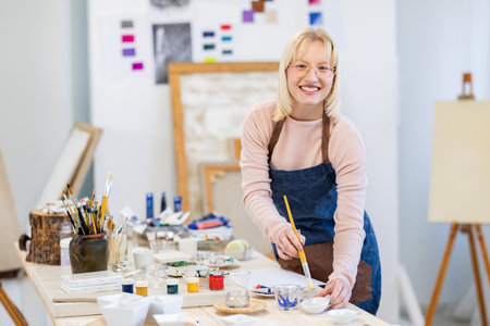 Portrait of smiling mature woman painting on canvas in art studio.の写真素材