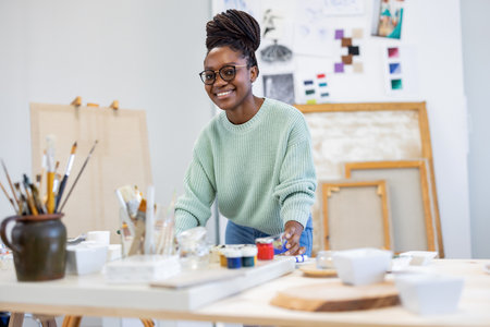 Portrait of smiling female artist standing at table in creative studio.の写真素材
