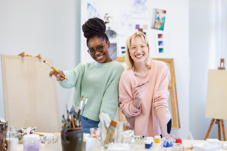Portrait of smiling female artist with colleague painting picture in art studioの写真素材