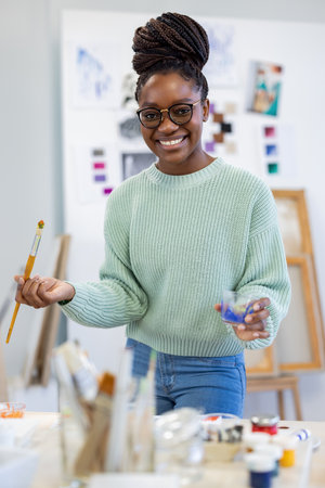 Portrait of smiling african-american female artist holding paintbrush in workshopの写真素材