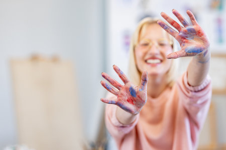 Smiling woman with hands painted in colorful paint at art studio.の写真素材