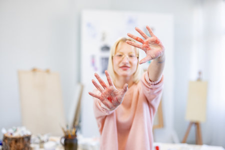 Mature female artist showing her hands to camera while standing in her studioの写真素材