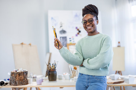 Portrait of smiling african american female artist holding paintbrush in studioの写真素材