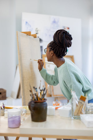 african american artist painting picture on easel at art studioの写真素材