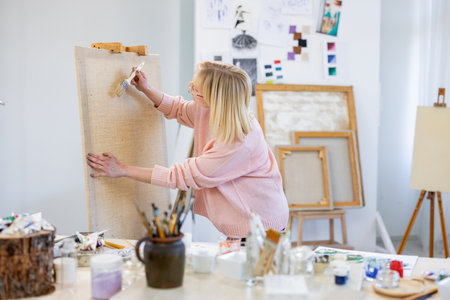 Portrait of young female artist painting picture on canvas in her studioの写真素材