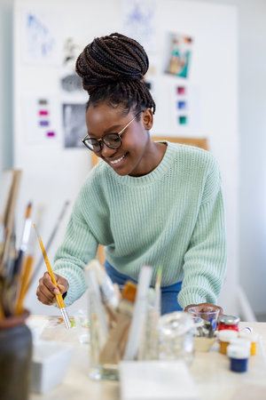 Portrait of smiling female artist painting picture in creative studio at deskの写真素材