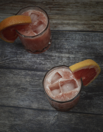 Two cold drinking glasses. Gin and tonic with red grapefruit on wooden background.の写真素材