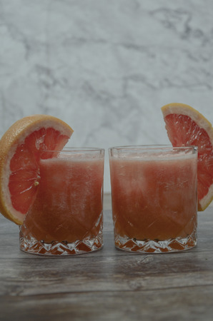 Two cold drinking glasses. Gin and tonic with red grapefruit on wooden background.の写真素材