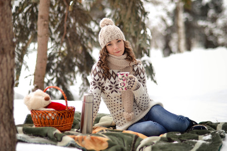 The beautiful,pretty, gool, cute, cheerful girl with mittens, hut, warm sweater with a cut of tea or coffe in the cold, snowy, frozen, big, nice and winter forest or parkの写真素材