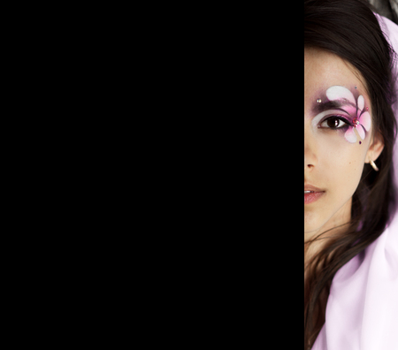 Inetresting, beautiful, attractive, nice, pretty girl.Unusual cover of fashion magazine, new book.Half face of beautiful girl with big dark black eye with creative, perfect makeup, pink and violet flowers, soft lips.Closeup portrait of half face. Nice makの写真素材