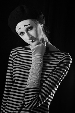 Emotional professional mime in stripped blacn and white shirt with black cap and white bow tie standing against black background in circusの写真素材