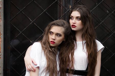 Two scared frightened horror girl in white dressing gown looking aside. Theme Halloween. Dark picture of two beautiful scared hiding girls with opened mouth on black window background.の写真素材