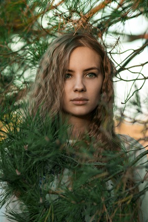 Stunning, gorgeous, striking, beautiful, dazzling, staggering, pretty, nice girl with big green.Very beautiful girl with green eyes stand in green fir-tree. Portrait of a very beautiful girl in green fir-trees, spruce, trees with curly, long, healthy hairの写真素材