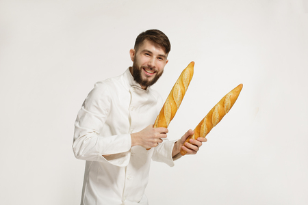 Handsome baker in uniform holding baguettes with bread shelves on the white background. Handsome man holding warm bread in his hands on white background.の写真素材