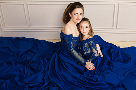 Mother and daughter hugging and looking at the camera. Happy loving family. Mother and daughter in beautiful long luxury blue dresses, makeup hairstyle. Fashion family portait. Generation relationshipの写真素材