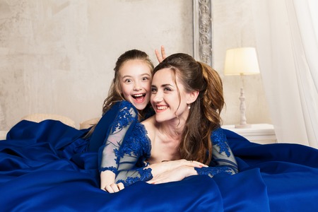 Mother and daughter hugging and looking at the camera. Happy loving family. Mother and daughter in beautiful long luxury blue dresses, makeup hairstyle. Fashion family portait. Generation relationshipの写真素材