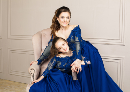 Mother and daughter hugging and looking at the camera. Happy loving family. Mother and daughter in beautiful long luxury blue dresses, makeup hairstyle. Fashion family portait. Generation relationshipの写真素材