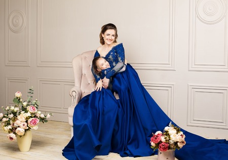 Mother and daughter hugging and looking at the camera. Happy loving family. Mother and daughter in beautiful long luxury blue dresses, makeup hairstyle. Fashion family portait. Generation relationshipの写真素材