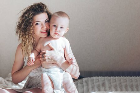 mother and babyboy sitting on bed and hugの写真素材