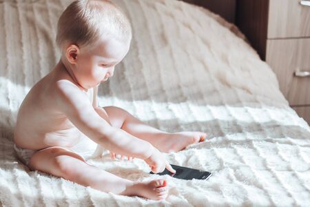 baby with the phone sitting on bedの写真素材