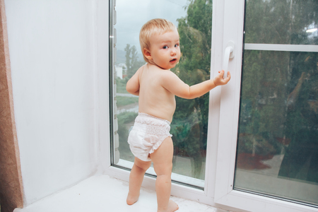 baby holding handle of window and looking at the streetの写真素材